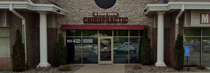 Front entrance of Cedar South Chiropractic clinic with a stone facade, red awning, and glass doors. The clinic name ‘Cedar South Chiropractic’ is displayed above the entrance