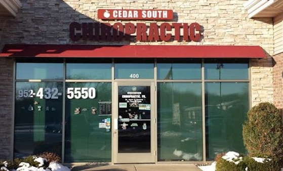 Front entrance of Cedar South Chiropractic clinic with large glass windows, a red awning, and a stone exterior. The sign above the door reads 'Cedar South Chiropractic' in bold red letters
