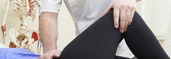 Physiotherapist performing a leg stretch on a patient wearing black leggings, with a skeleton model visible in the background