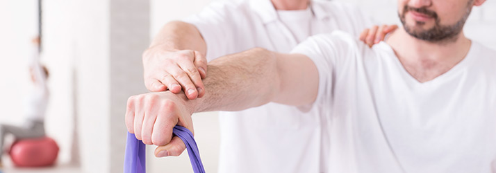 Close-up of a physical therapy session where a therapist assists a person in performing an arm exercise using a purple resistance band